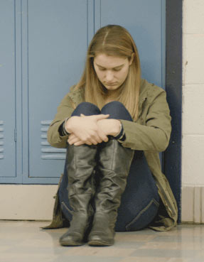 Young girl cradling legs in a school hallway.