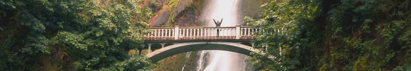 Person posing on walk bridge in front of waterfall