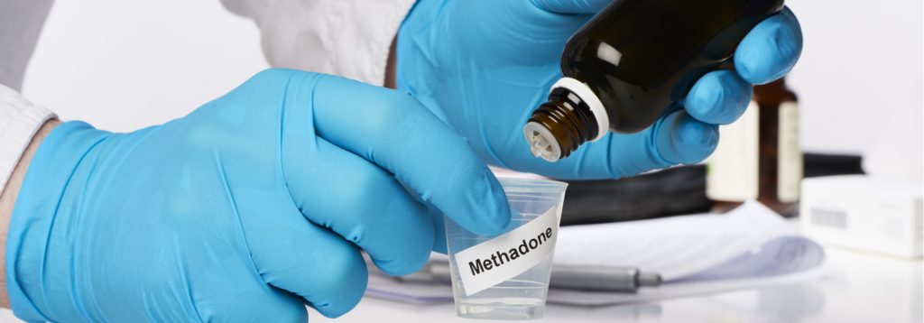 doctor wearing blue gloves dripping methadone into small cup